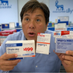 A man in a pharmacy holds up various boxes of medication labeled with different prices, including "$499," "$99," and "$39," with Novo Nordisk and Eli Lilly branding visible in the background.